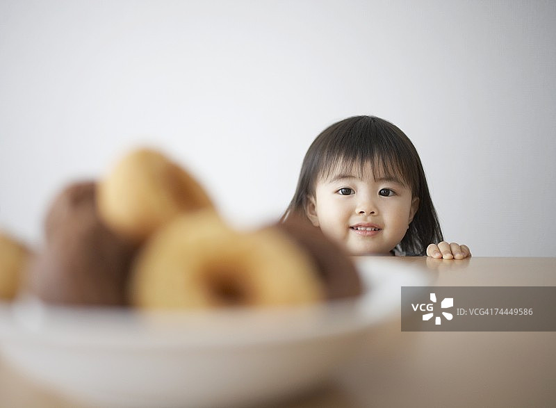 日本女孩在桌子上的甜甜圈前微笑图片素材