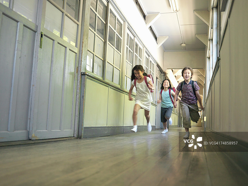 三个孩子(7-9岁)在学校走廊里奔跑图片素材
