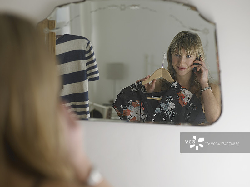 年轻女人用手机对着镜子里的连衣裙微笑图片素材