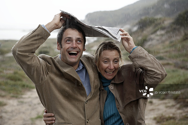 中年夫妇在海滩附近用报纸遮雨，欢笑图片素材