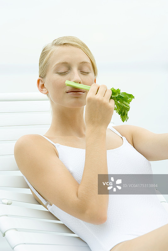 身穿泳衣坐在躺椅上，闻着芹菜的少女图片素材