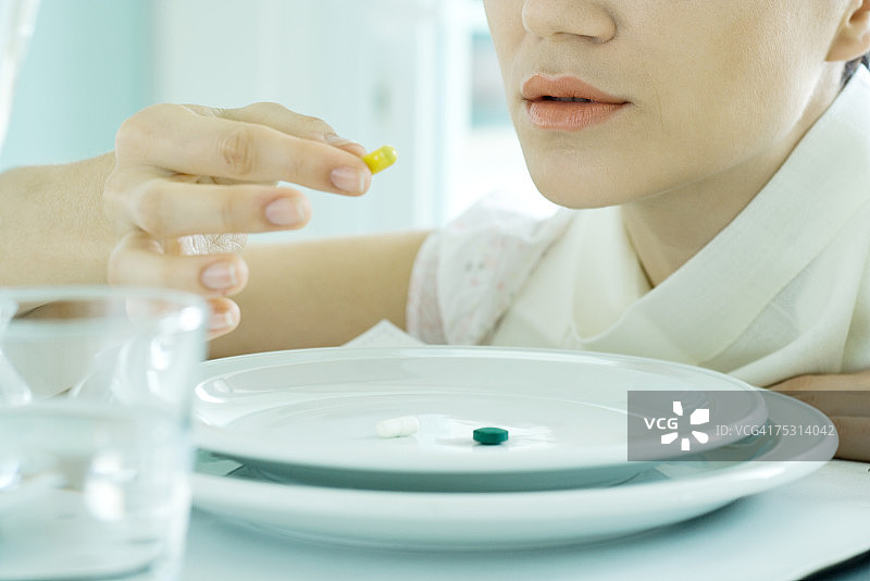 女人坐在摆好的桌子旁，吃盘子里的维生素图片素材