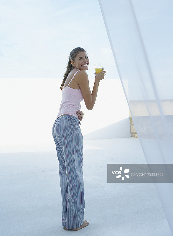 年轻女人手持果汁杯，微笑，侧面人像图片素材