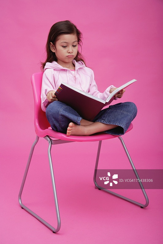 坐在椅子上皱着眉头看书的女孩图片素材