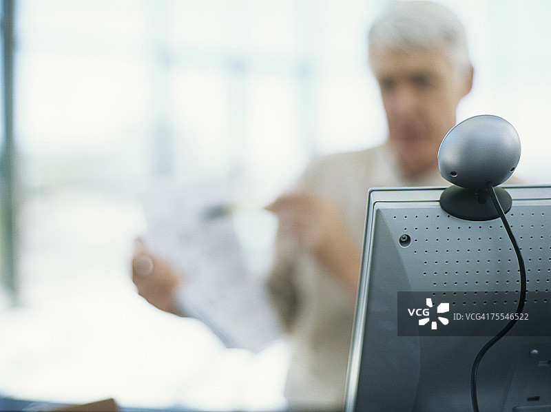 商人拿文件，焦点在前景的网络摄像头上图片素材