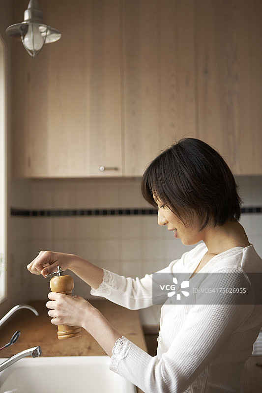 女人在厨房水槽边使用胡椒研磨器图片素材