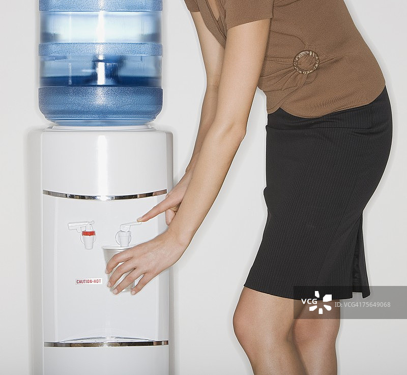在饮水机旁倒水的商务女性图片素材