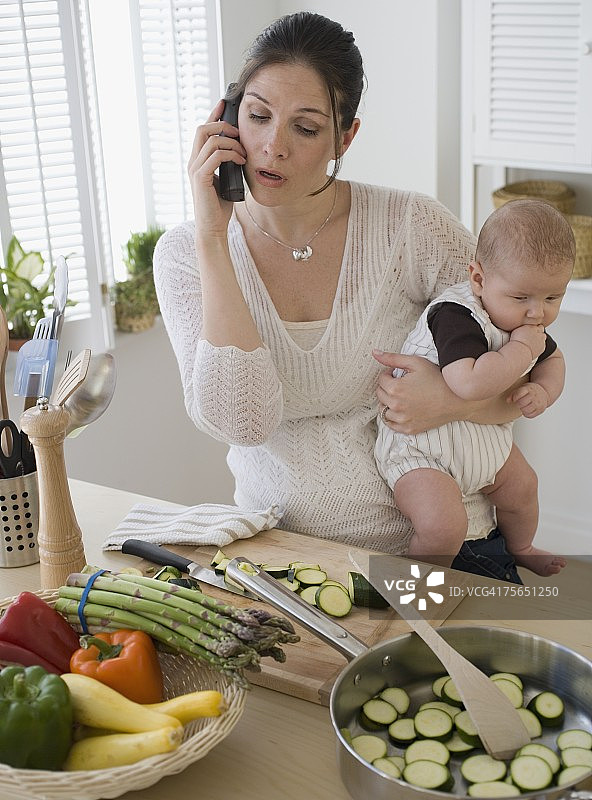 母亲抱着婴儿，打电话和做饭图片素材