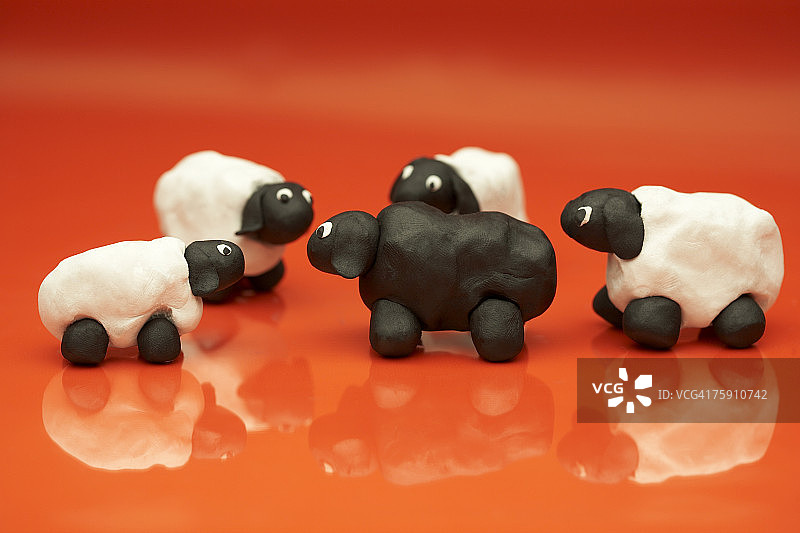红色背景上用粘土制成的四只白羊和一只黑羊图片素材
