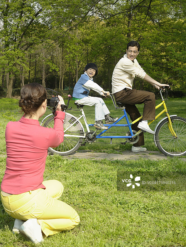 女人拍摄丈夫和儿子骑双人自行车图片素材