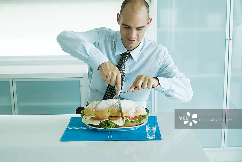 男人用刀叉切一个大三明治图片素材