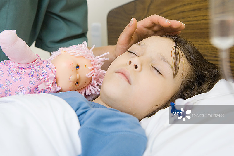 在医院病床上睡觉的女孩，女人将手放在女孩的额头上图片素材