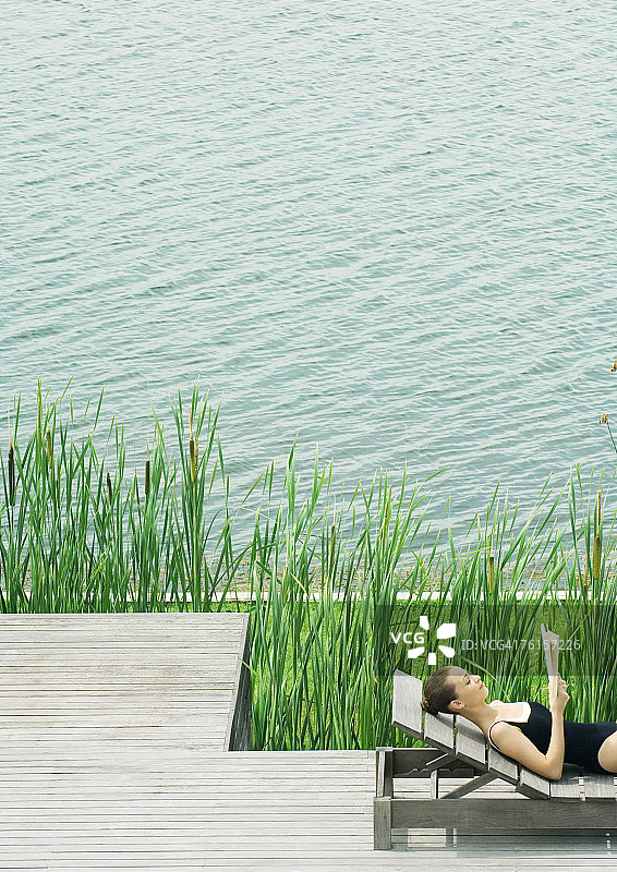 女人躺在躺椅上，在湖边阅读图片素材