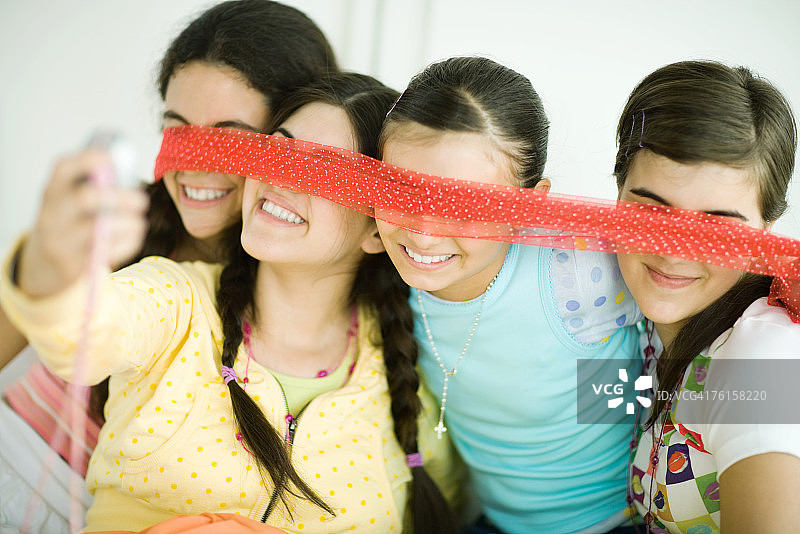四个年轻女子用围巾遮住眼睛，一人用手机拍照图片素材