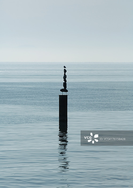 堆在水中木桩上的石头，顶部栖息着一只鸟图片素材