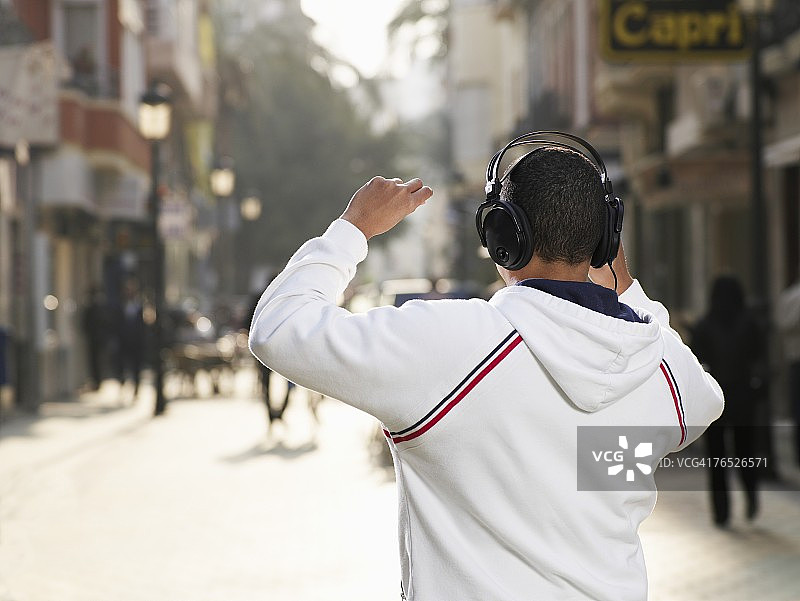 戴着耳机站在街上的年轻男人（后视图）图片素材