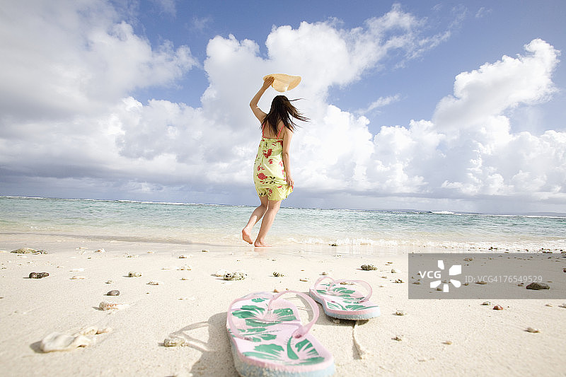 在海滩上的年轻女人，前景是凉鞋特写图片素材