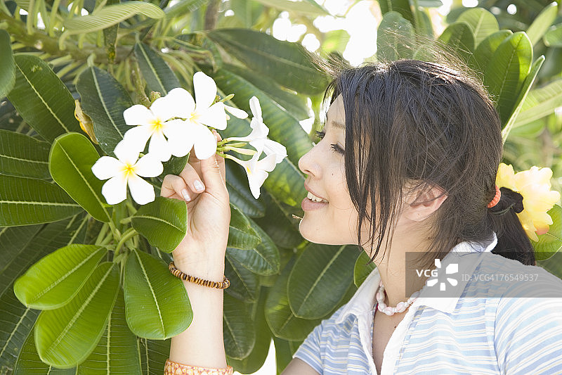 年轻女人闻树上的花，侧视图，头部和肩膀图片素材
