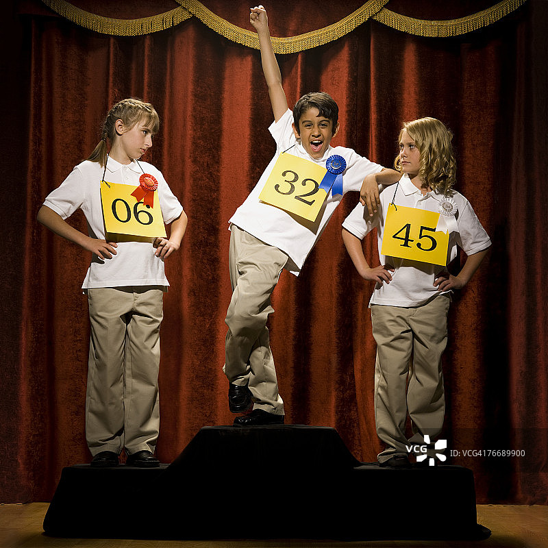 三个孩子在领奖台上微笑，带着绶带图片素材