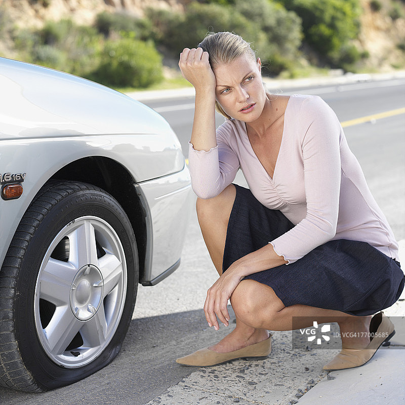 女人蹲在有爆胎的车旁图片素材