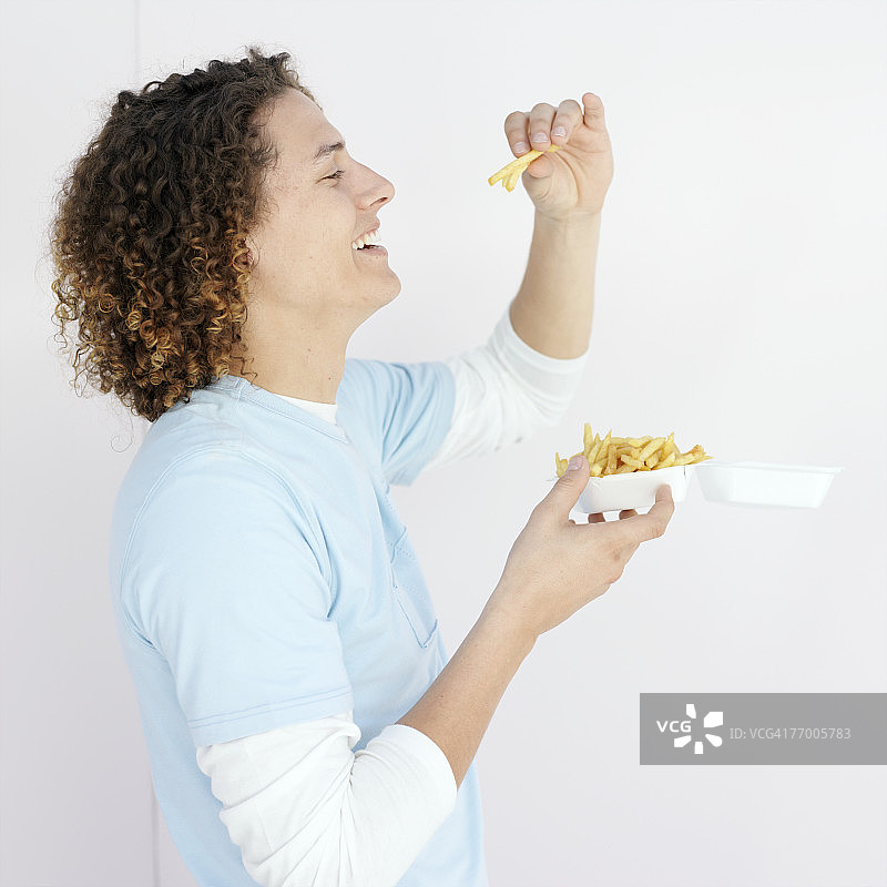 吃塑料托盘里炸薯条的年轻男人，侧面半身像图片素材