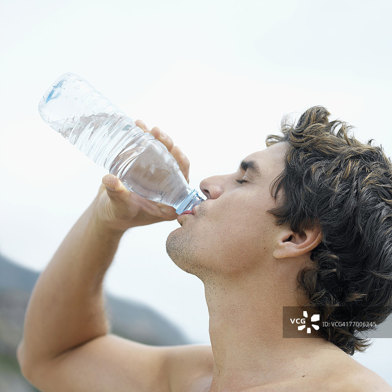 在户外从瓶子里喝水的年轻男人，侧面，头部和肩膀图片素材