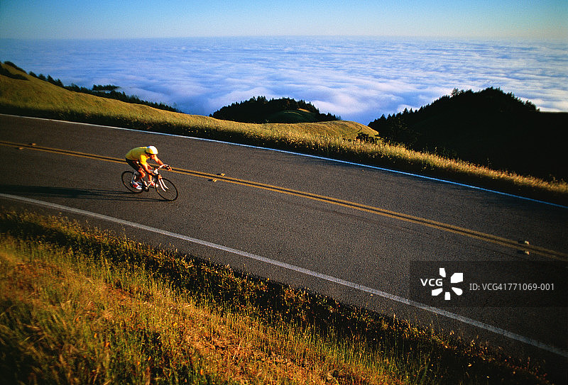 戴头盔的男人在路上骑自行车，背景是雾气笼罩的海岸线图片素材