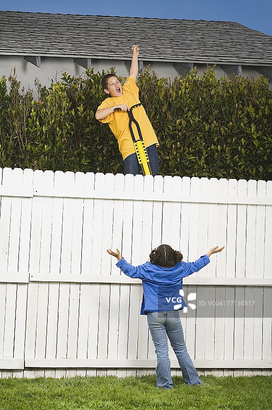 混血男孩尝试用弹簧单高跷跳过栅栏图片素材