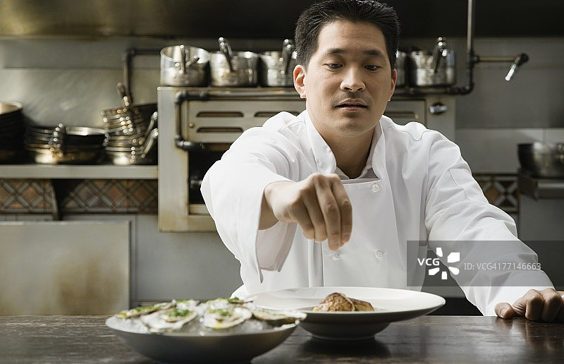 亚洲男厨师正在调味食物图片素材