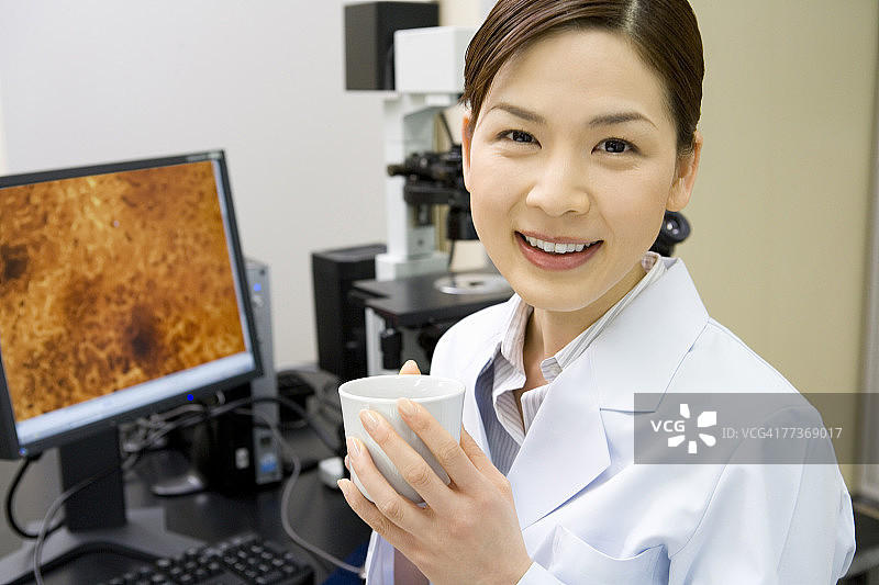 女科学家在实验室手持咖啡杯的正面肖像，面带微笑看向镜头图片素材