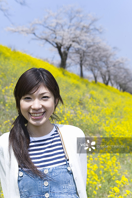 站在油菜花田中微笑看着镜头的女人肖像，日本图片素材
