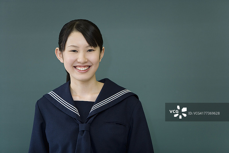 站在黑板前微笑看着镜头的少女肖像，绿色背景图片素材
