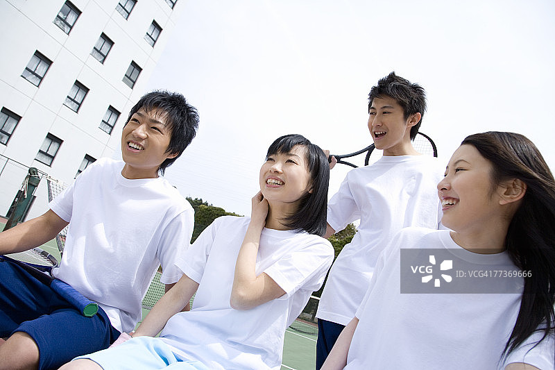 四名青少年坐在网球场的长凳上，拿着球拍图片素材