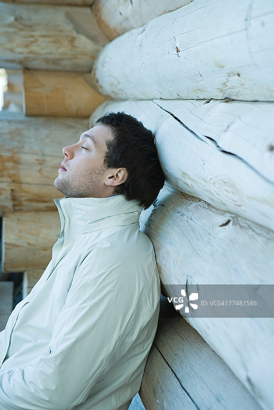 年轻男人靠在小木屋上，闭着眼睛图片素材