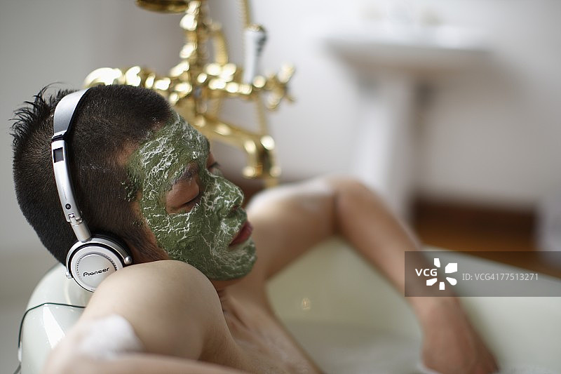 在浴缸里戴着面膜听音乐的男子图片素材