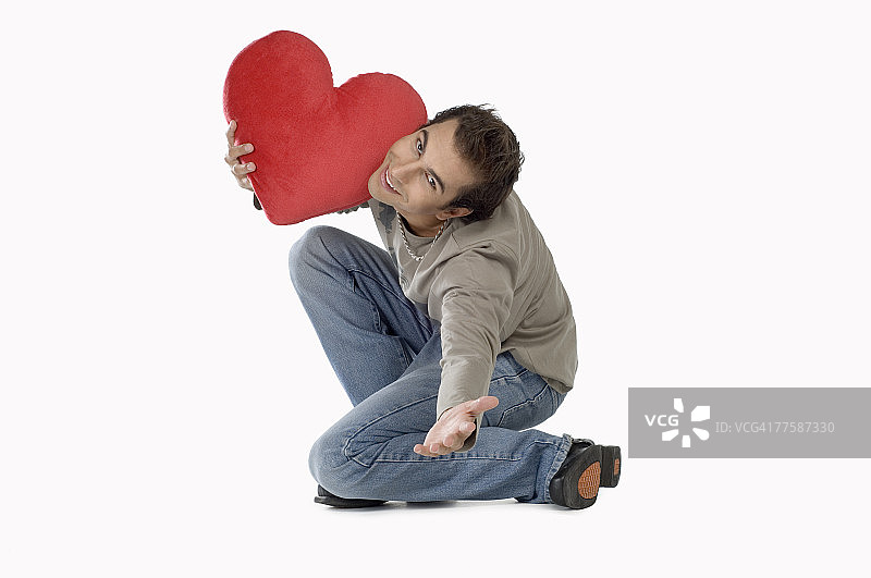 拿着心形靠垫微笑的年轻男人肖像图片素材