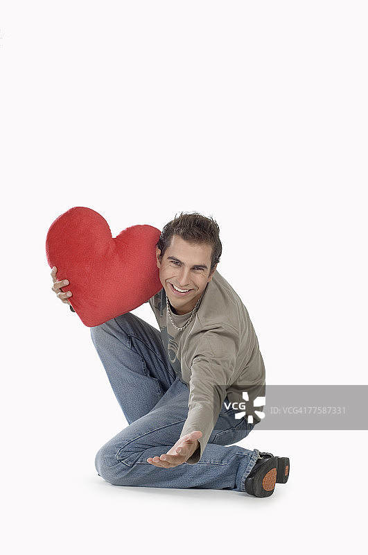 拿着心形靠垫微笑的年轻男人肖像图片素材