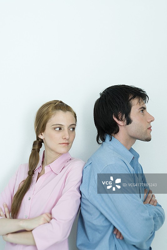年轻情侣背靠背站立，交叉双臂，女子回头看，半身像，肖像图片素材