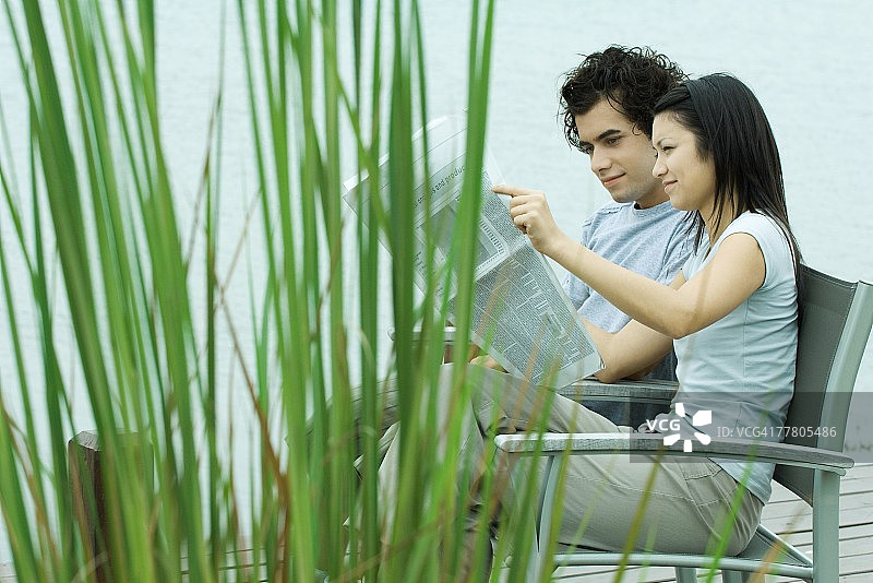 年轻夫妇在湖边一起读报纸图片素材