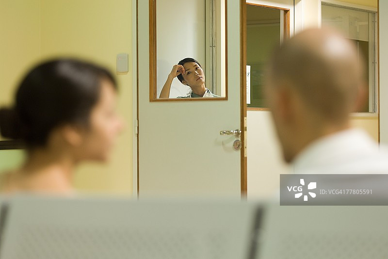 在医院候诊室透过窗户看镜头的女人，前景是成年人图片素材