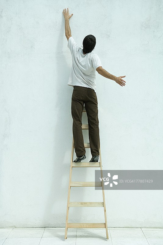 站在梯子上，举起手臂，后视的男人图片素材
