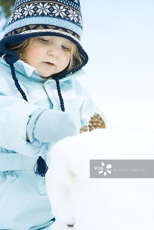 穿着冬装的幼儿女孩堆雪人图片素材