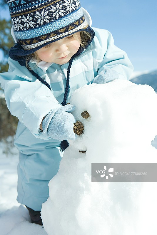 穿着冬装的幼儿女孩堆雪人图片素材