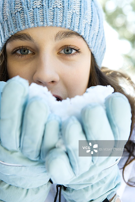 少女戴着手套从手中吃雪，看着镜头，特写图片素材