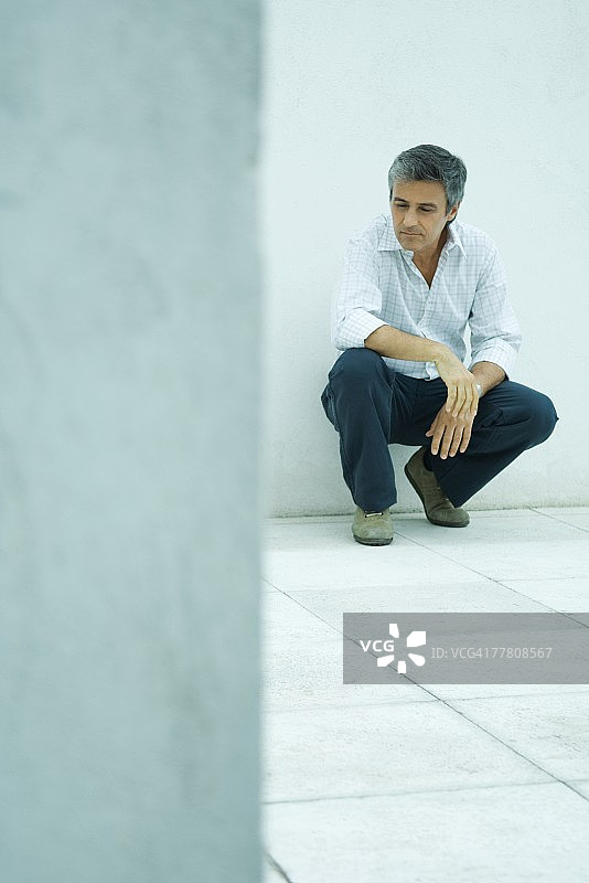 蹲下、向下看的中年男人全身像图片素材