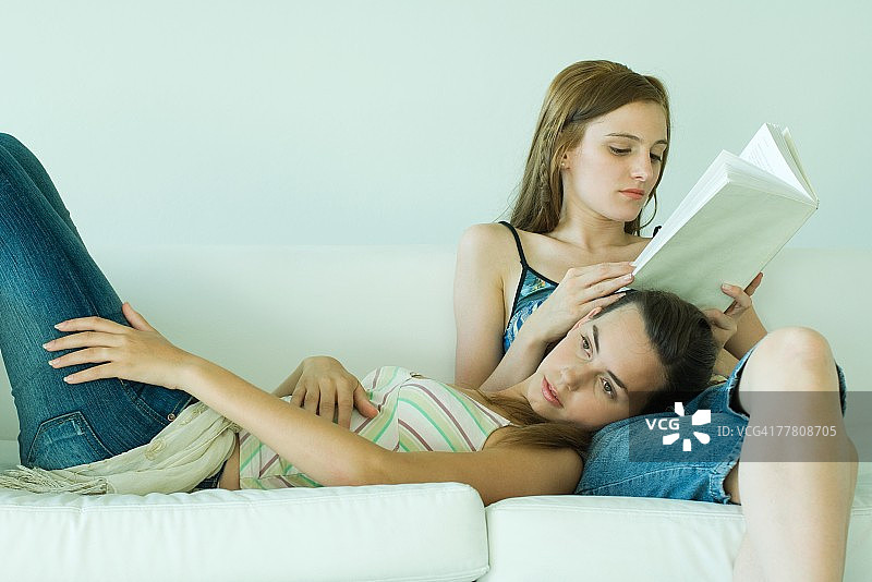 年轻女人在沙发上看书，朋友把头靠在她腿上图片素材