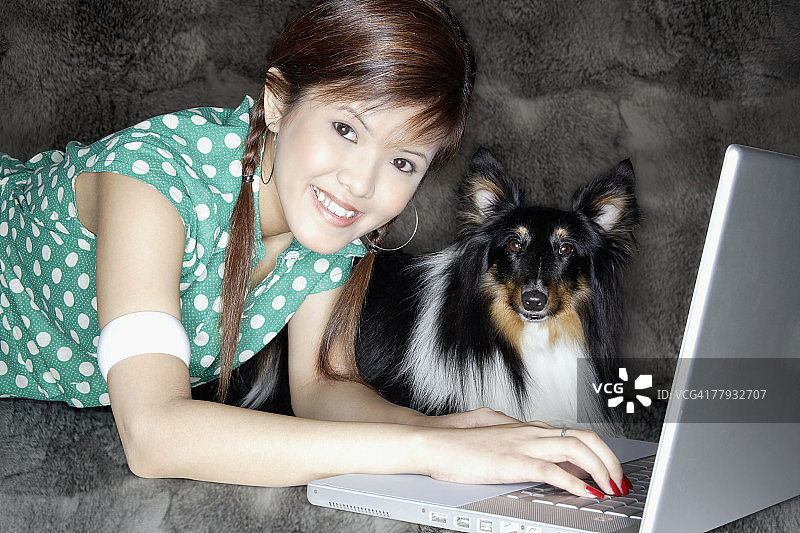 抱着小狗在室内使用笔记本电脑的女孩图片素材