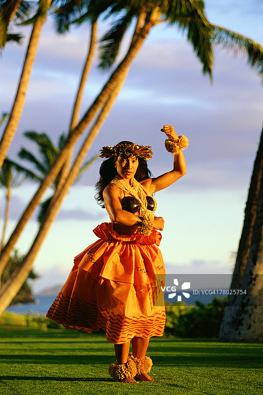 夕阳下，女人在户外海边跳草裙舞，穿着夏威夷草裙和贝壳花环图片素材