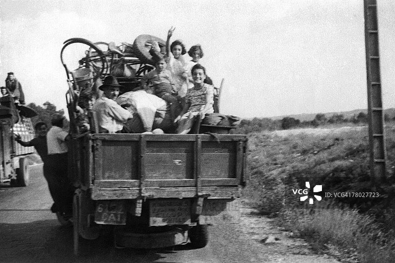 大约1900年代，一个男人和孩子们坐在旧卡车后座上，两个人坐在卡车侧面图片素材
