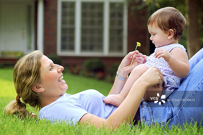 母亲仰卧与坐在她肚子上的女儿互动侧视图图片素材